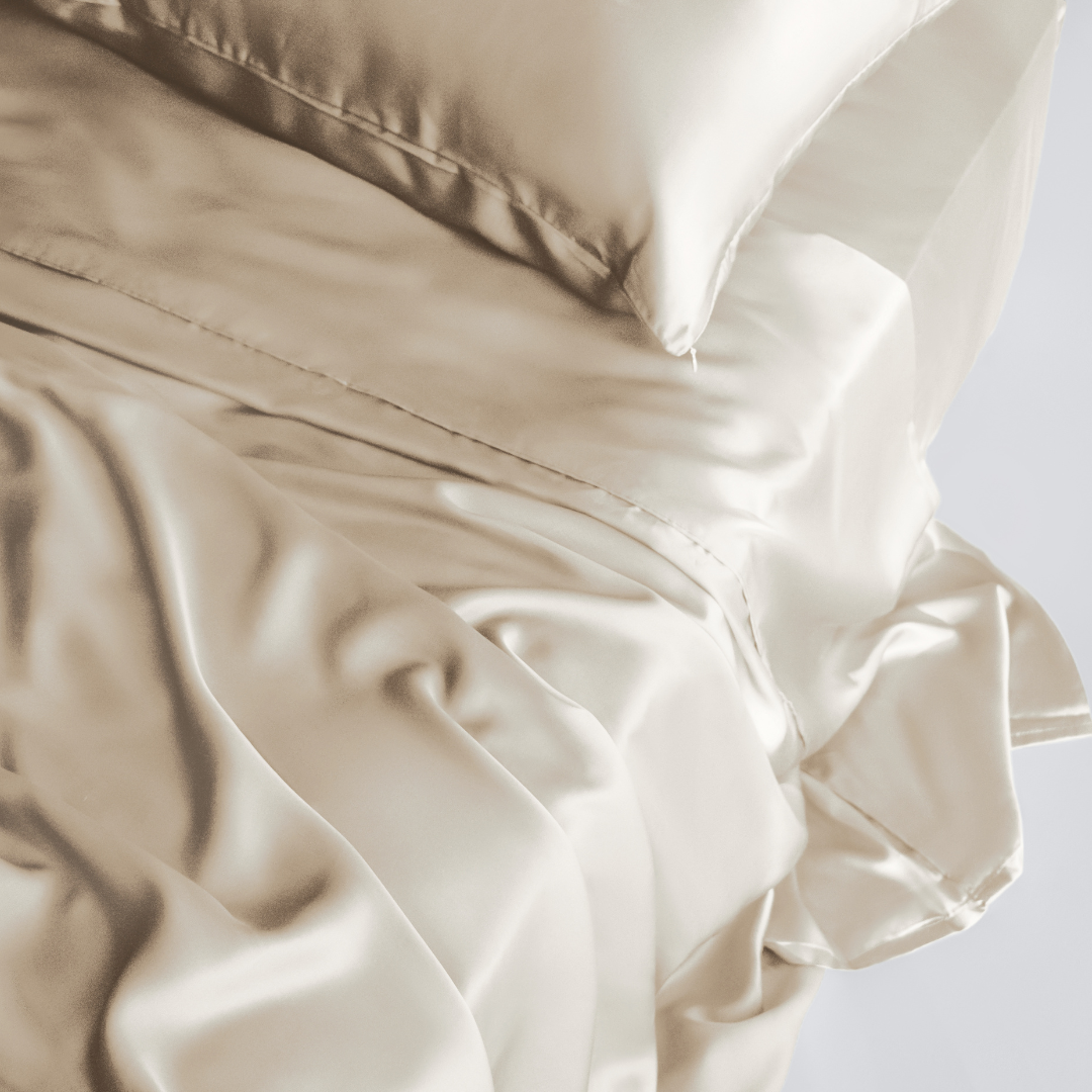 A close-up of a neatly made bed featuring the Complete Sheet Set (4-Piece) in cream, with silky soft, smooth fabric and a subtle sheen for a luxurious look.