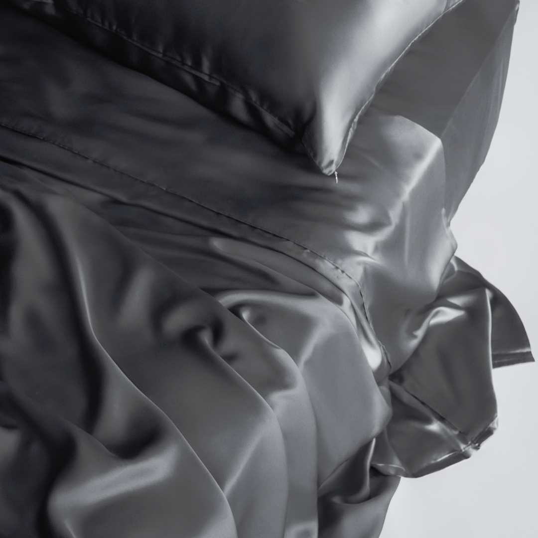 A close-up of the Complete Sheet Set (4-Piece) in shiny black, featuring rumpled silky soft sheets and a matching pillow for a smooth, luxurious look.