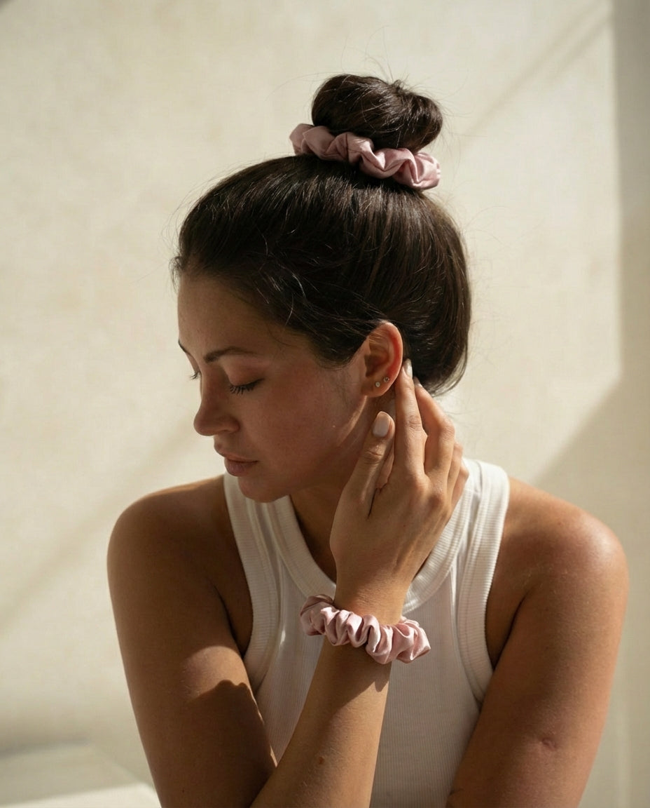 Woman with pink scrunchies in her hair and on her wrist against a neutral background