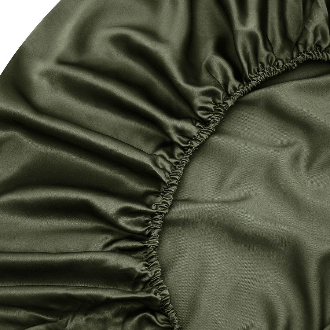 Close-up of the Fitted Sheet Set in dark green, featuring silky soft, smooth, and slightly shiny fabric with gathered elastic edges.
