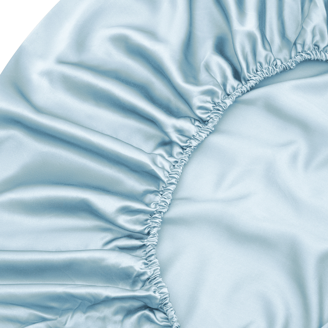 Close-up of the Fitted Sheet Set in light blue, featuring silky soft fabric with gathered elastic edges, highlighting its smooth, shiny texture and delicate wrinkle details.