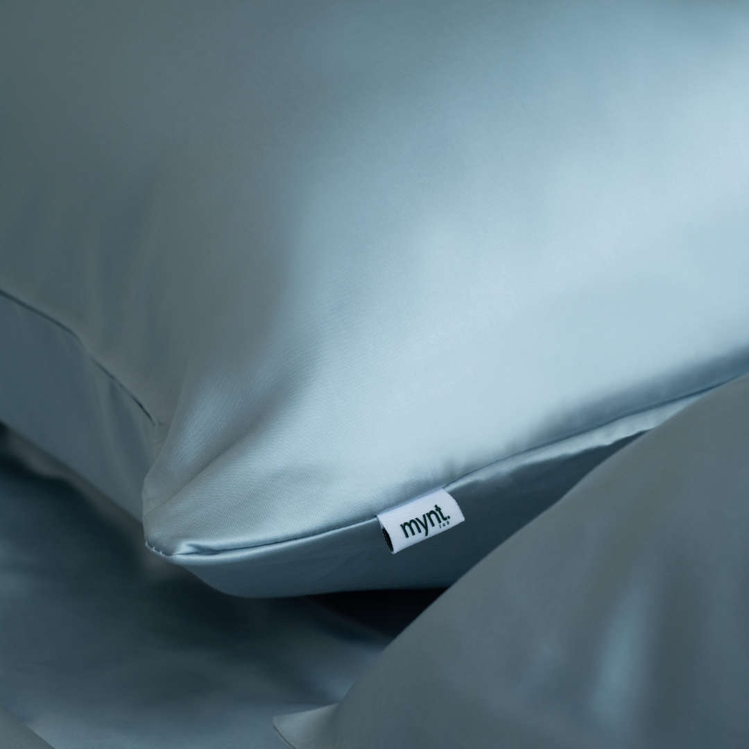 A close-up of a light blue silky pillow with a "mynt lab" tag rests on silky, matching fitted sheets from the Fitted Sheet Set.