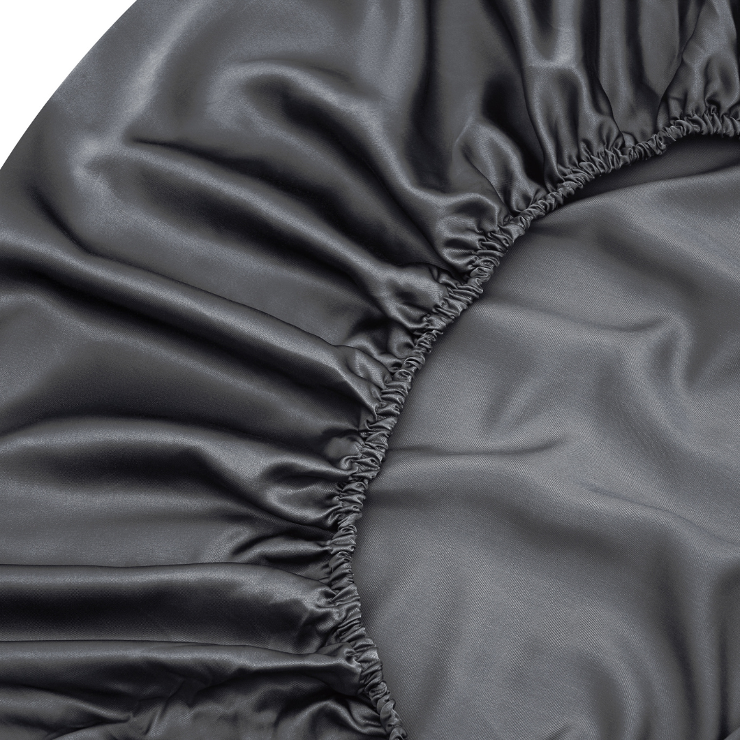 Close-up of the Fitted Sheet Set (3-Piece) in dark gray satin, featuring gathered elastic edges, silky soft and shiny fabric, plus elegant ruffled corner details—ideal for anyone wanting smooth, luxurious sheets.