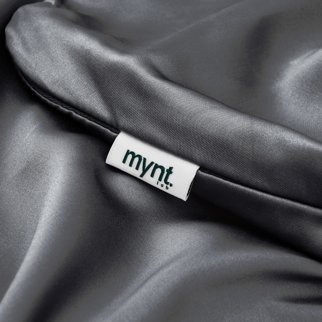 A close-up of the smooth, shiny gray Fitted Sheet Set (3-Piece), famous for its silky softness, featuring a white tag with "mynt" in lowercase black letters.