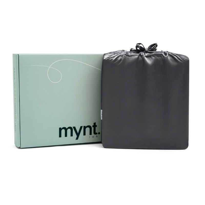A light green mynt lab box stands upright beside a neatly folded charcoal-coloured drawstring bag against a white background - perfectly showcasing the Fitted Sheet Set (3-Piece).