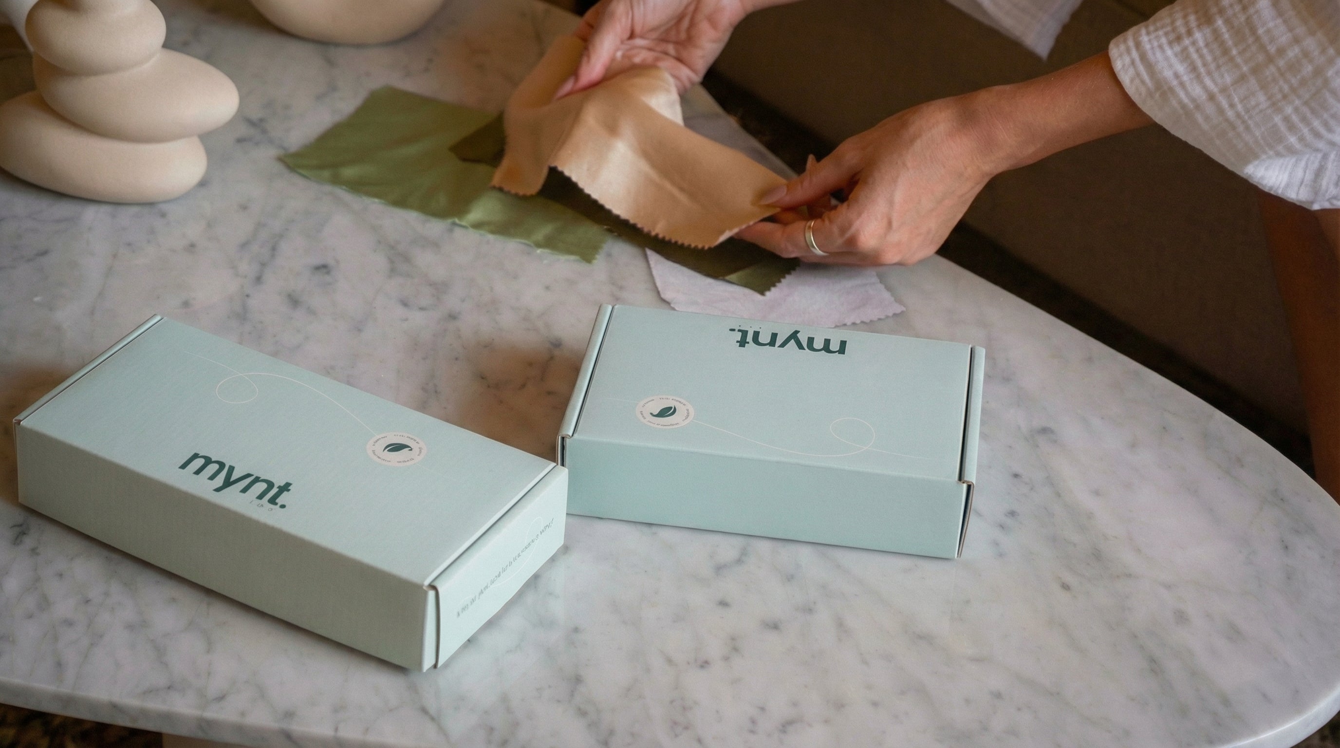 Person placing a fabric swatch next to two mynt lab boxes on a marble table surface