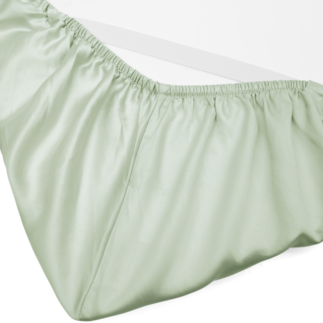 A close-up of a sage green fitted silky sheet with gathered elastic edges, displayed on a white background.