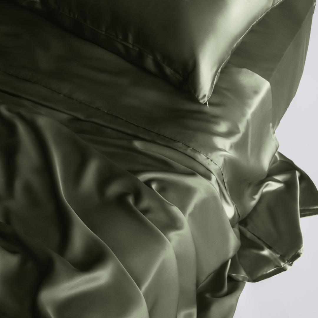 A close-up of the Mynt Lab MyntFusion™ Complete Sheet Set (4-Piece) in shiny olive green satin and matching pillow, showcasing their silky soft, smooth texture—perfect for adding elegance and comfort to any bedroom.