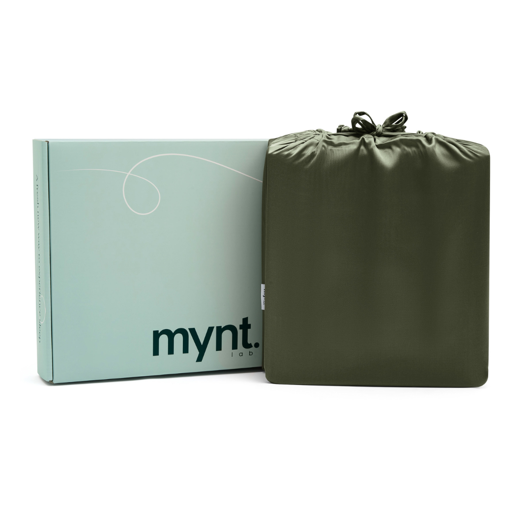 A light blue box labeled "mynt lab" is beside an olive green drawstring pouch, both included with the Fitted Sheet Set- ideal for keeping your silky soft sheets organised.