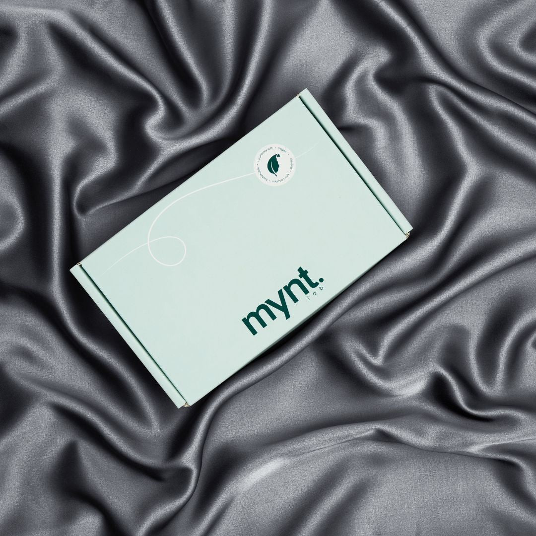 A mint green rectangular Mynt Lab Pillowcase box rests on flowing, shiny charcoal silky fabric, creating a luxurious display that evokes beauty sleep and promises hydrated skin.