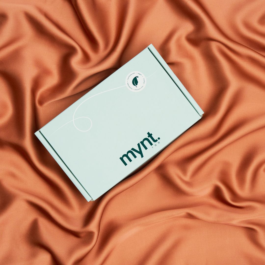 A mint green Mynt Lab Pillowcase box sits on smooth terracotta silky fabric. The simple Mynt Lab logo and a small circular sticker make it perfect for elevating your beauty sleep routine.