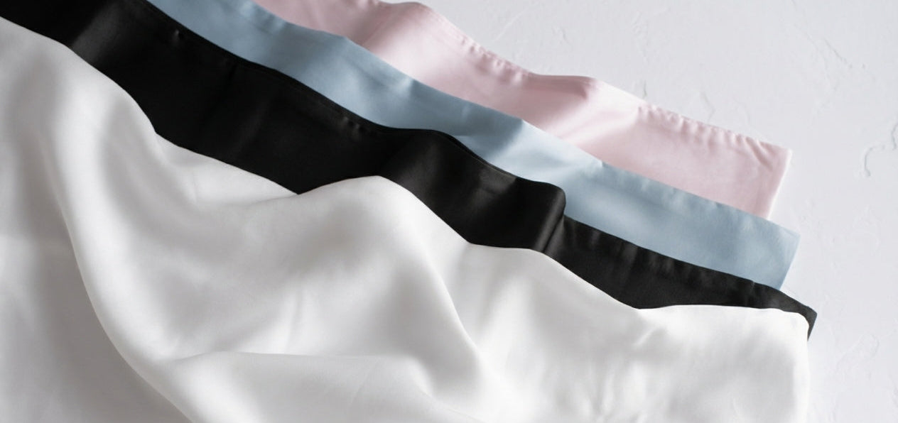 Four silky pillowcases in black, white, pink  and blue on a light grey background