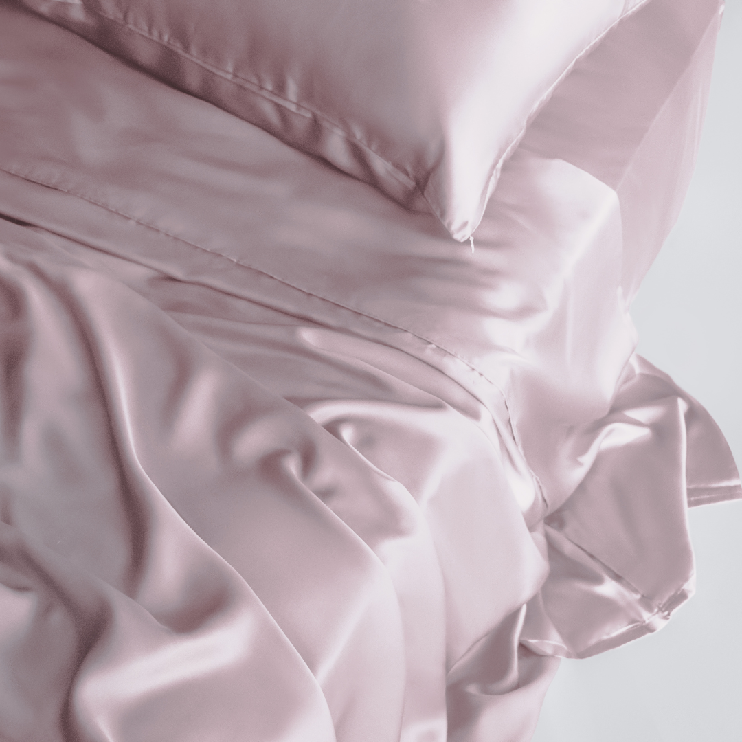 Close-up of a neatly made bed with smooth, shiny, pale pink Pink Sheet Set, featuring silky soft sheets and pillowcases gently draped and slightly rumpled.