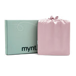 The Mynt Lab MyntFusion™ Complete Sheet Set (4-Piece) for hot sleepers, in folded pink satin, comes in a drawstring bag beside a light green box with "mynt." printed in black on the front.