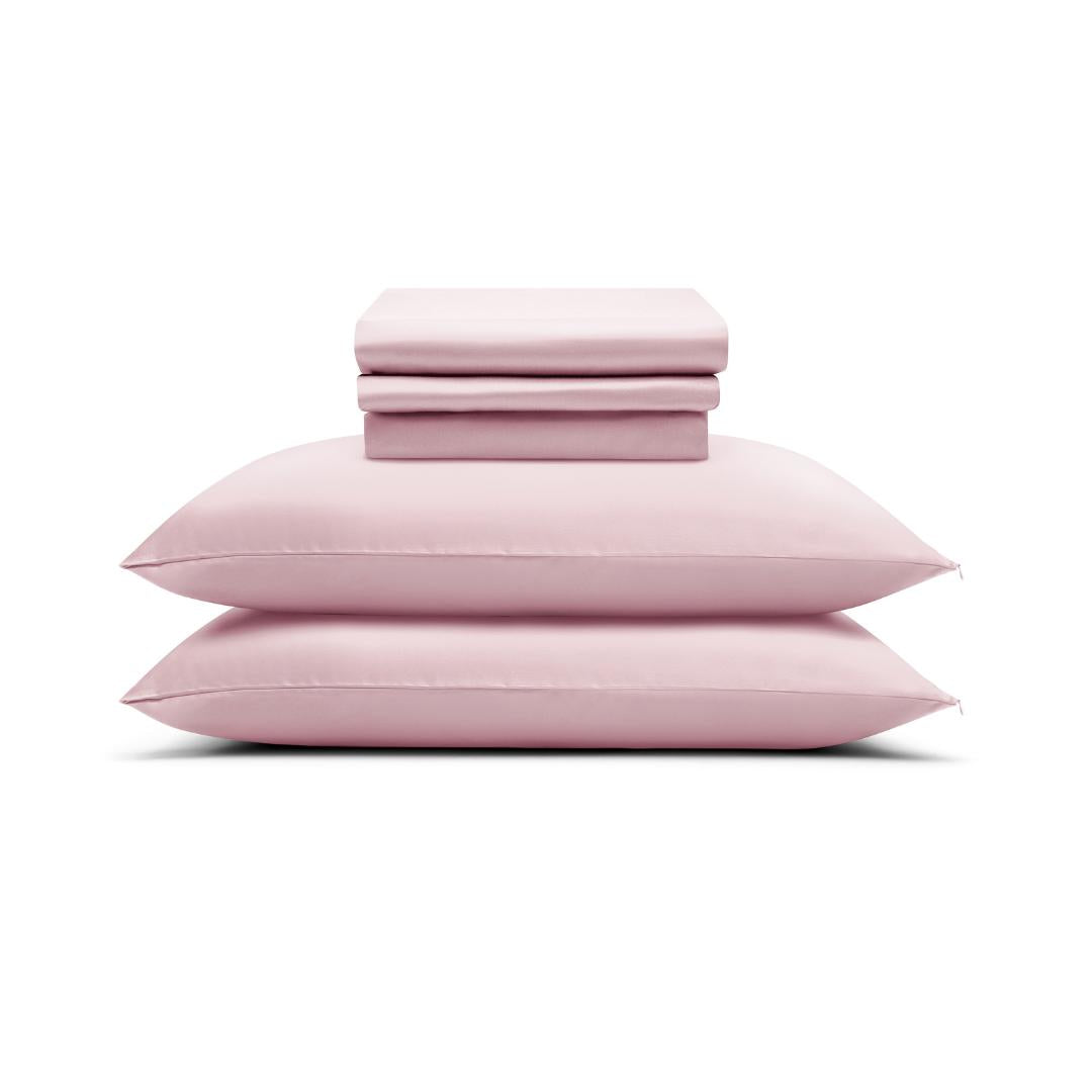 The Pink Sheet Set features silky soft, pale pink bed linens - including two pillows and a folded sheet set - neatly stacked on a white background.