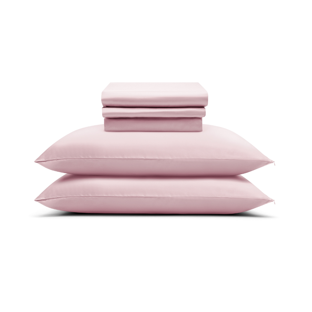 The Pink Sheet Set features silky soft, pale pink bed linens - including two pillows and a folded sheet set - neatly stacked on a white background.
