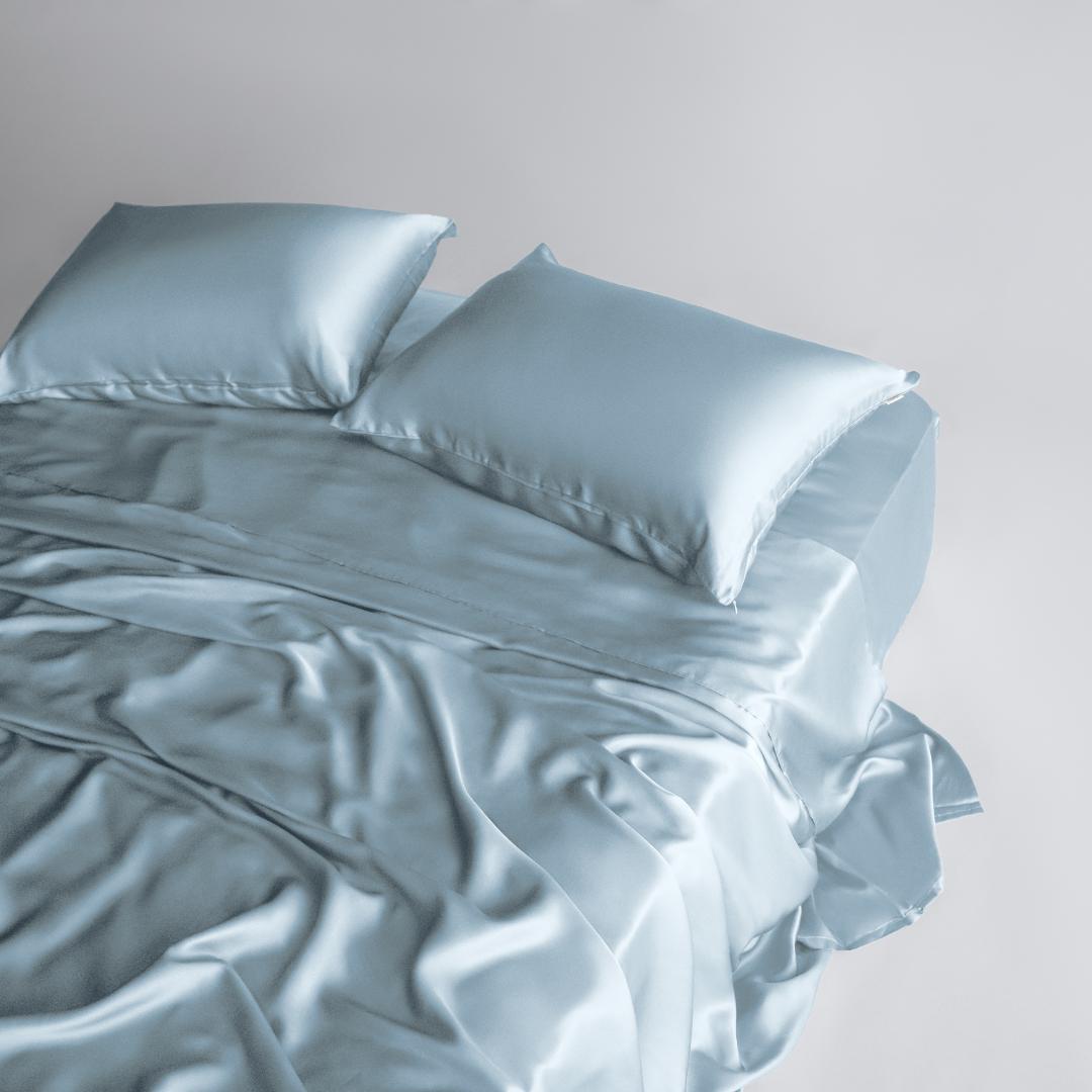 A neatly made bed with the Mynt Lab MyntFusion™ Complete Sheet Set (4-Piece) in light blue, featuring silky soft sheets and two matching pillows, smoothly draped over the bed on a light background.