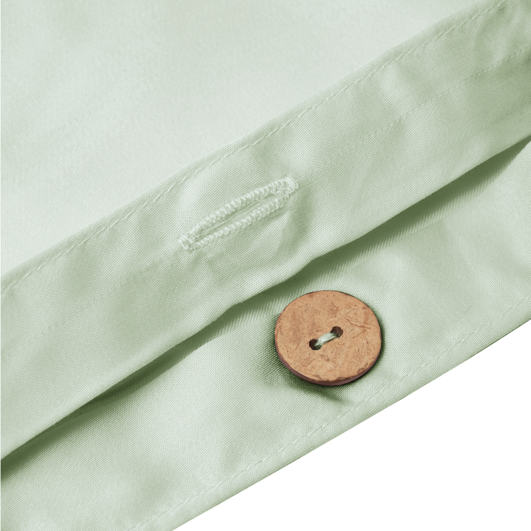 Close-up of a light green fabric with a brown wooden button and a stitched buttonhole, suggesting part of a garment or a pillowcase opening.