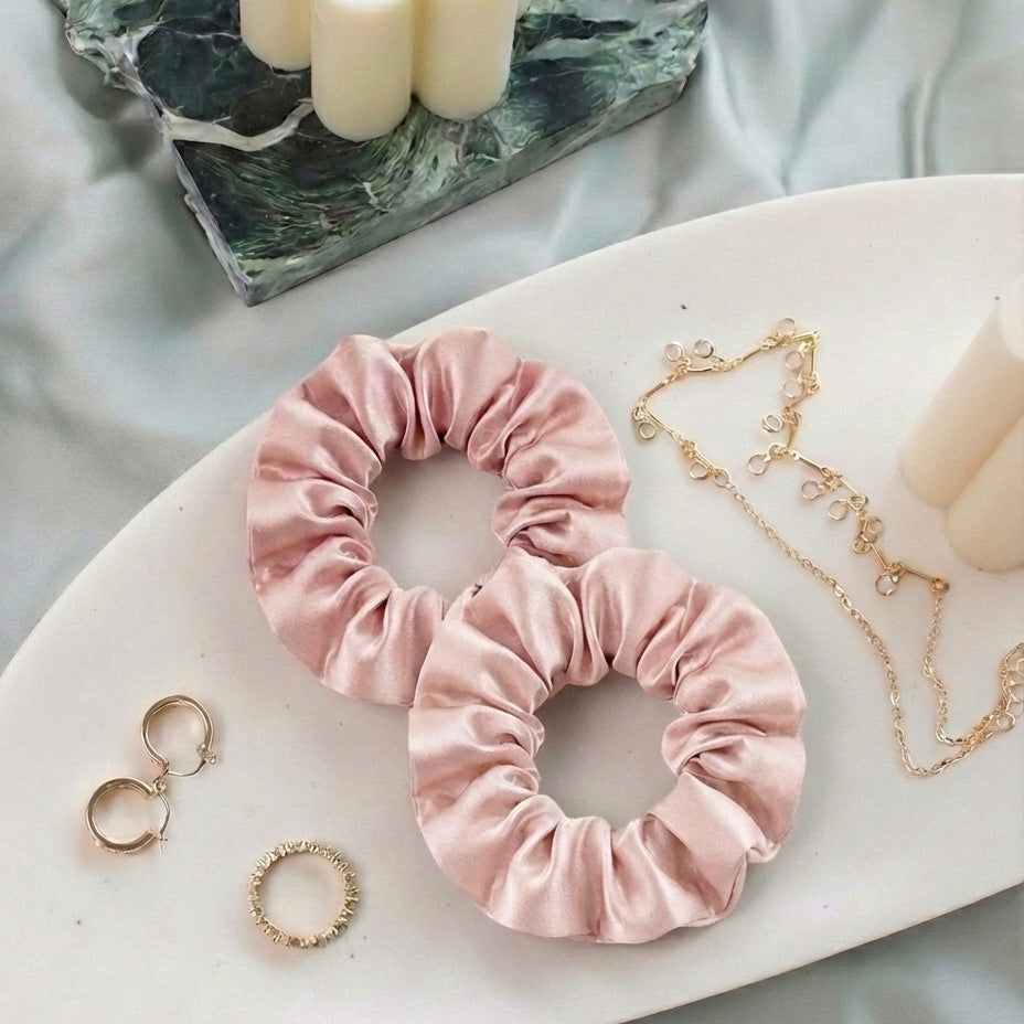 Pink scrunchies on a marble tray with jewelry and candles.