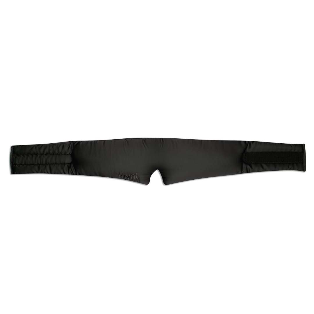 The Sleep Mask is a black, padded, adjustable strap with Velcro ends and a small central cutout for light blocking, featuring subtle stitched detailing. Laid flat on a white background, it's designed to promote deep sleep.