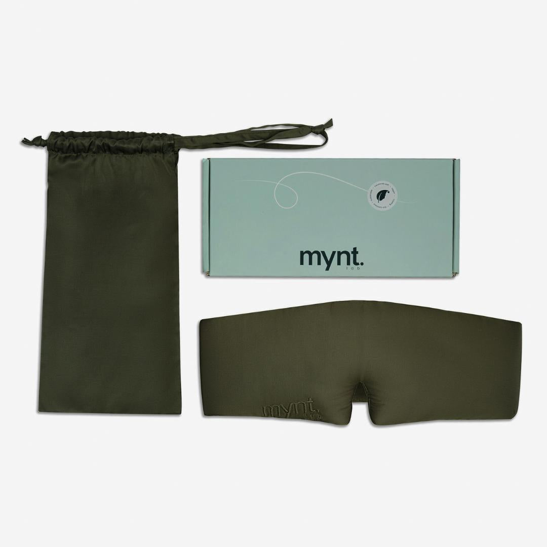 An olive green Sleep Mask for blocking light, shown with a matching drawstring pouch and a mint-green box labeled "mynt lab.", is displayed on a white background.
