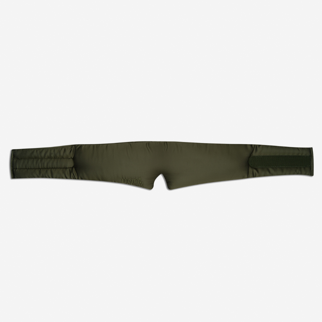 The Sleep Mask, in padded olive-green, features two wide straps and a center notch for maximum light blocking and deep sleep support, shown laid flat on a white background.