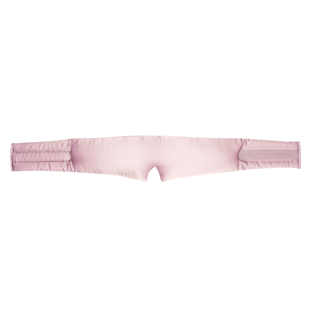 The Sleep Mask is a light pink, padded headband with two adjustable Velcro straps on each end, designed to block light and promote deep sleep. It is shown laid flat on a white background.