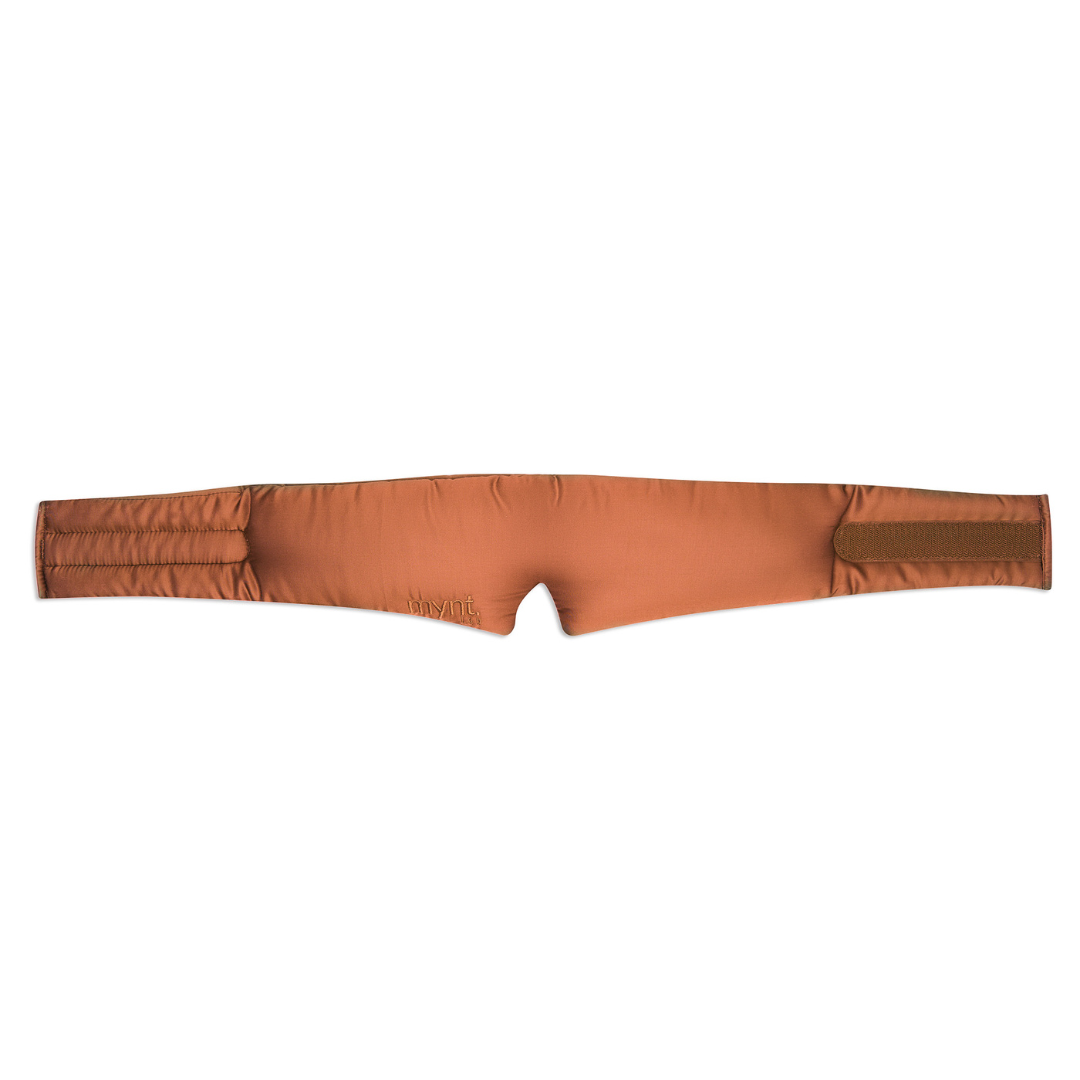 The Sleep Mask is a terracotta, padded fabric band with a contoured centre notch to block light and velcro fasteners on both ends, shown laid flat on a white background - ideal for deep sleep.