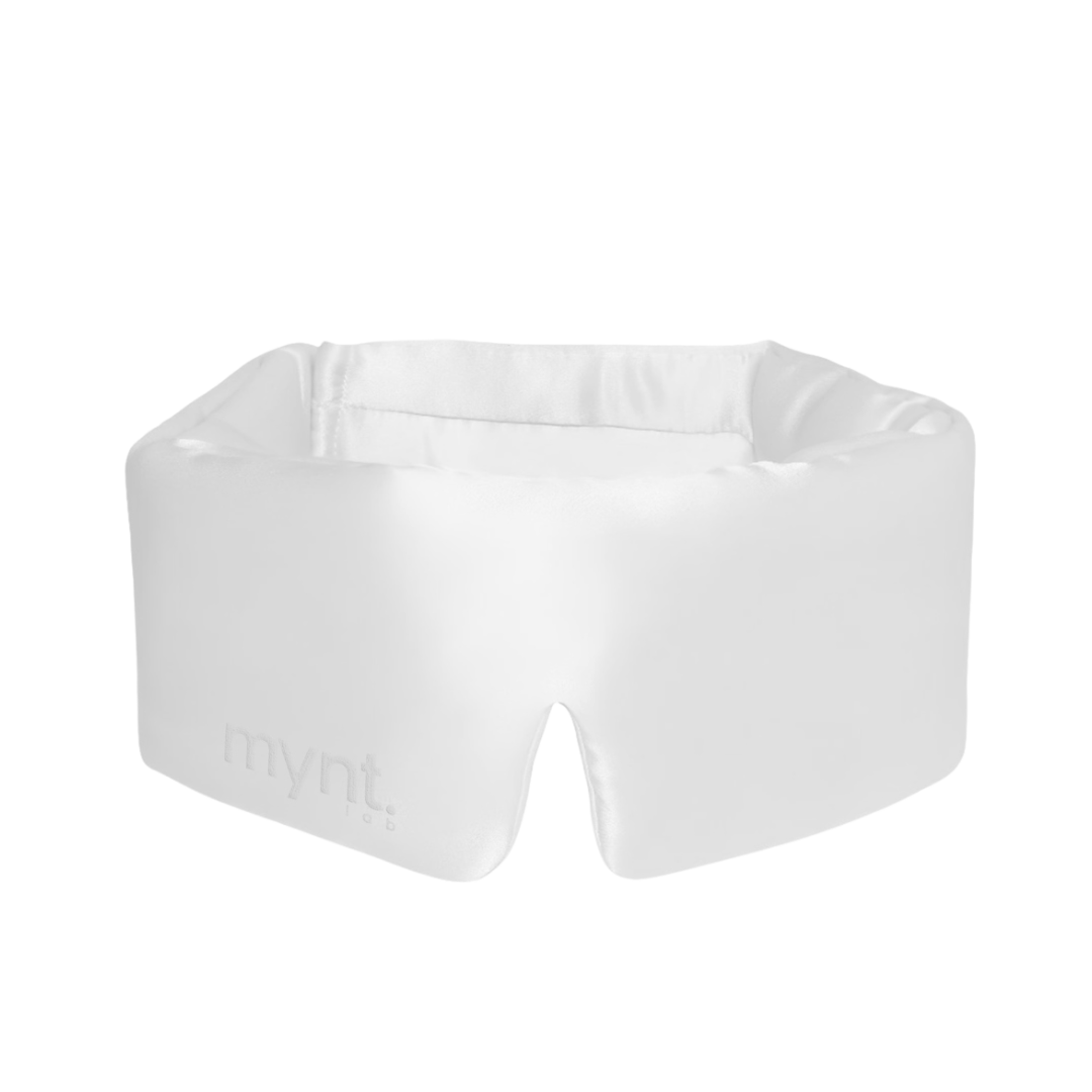 The Sleep Mask is a white, padded mask with a subtle mynt lab logo, designed to fit comfortably around the eyes and nose. Its slight sheen and secure fit help block light, making it ideal for deep sleep and relaxation.