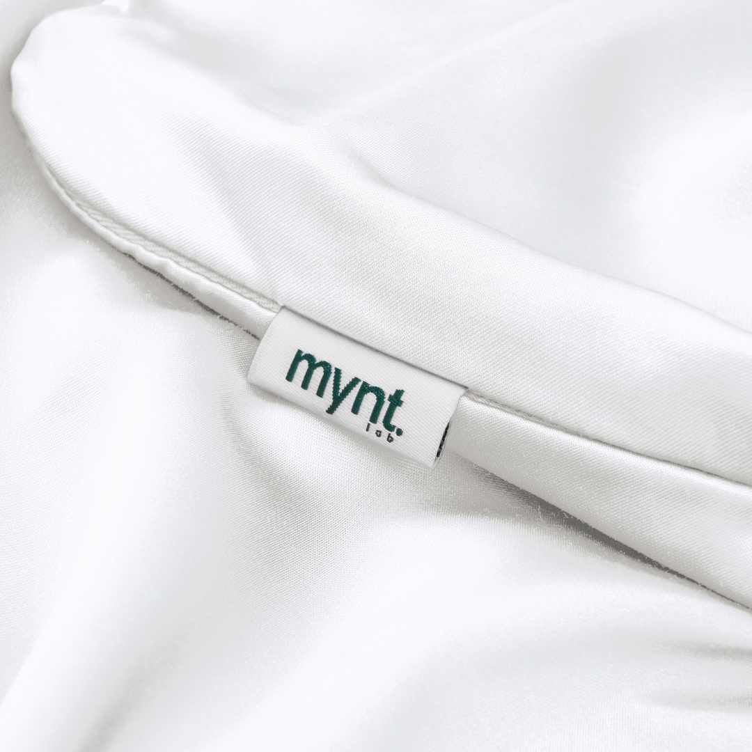 A close-up of the Fitted Sheet Set's white fabric features a small white tag in the seam with mynt lab in black text - an elegant detail on these silky soft sheets.