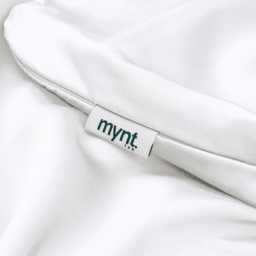 A close-up of the Fitted Sheet Set's white fabric features a small white tag in the seam with mynt lab in dark green text - an elegant detail on these silky soft sheets.