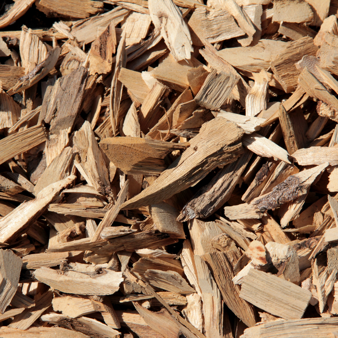 A close-up view of a pile of light brown wood chips with jagged edges and various sizes, often used for mulch or as a landscaping material.