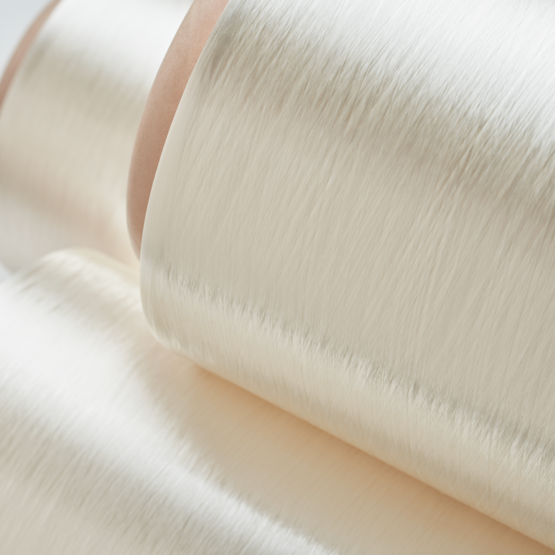 Close-up of smooth, shiny, white synthetic fiber rolls with a silky texture, showing fine, even threads and a soft sheen under gentle lighting.